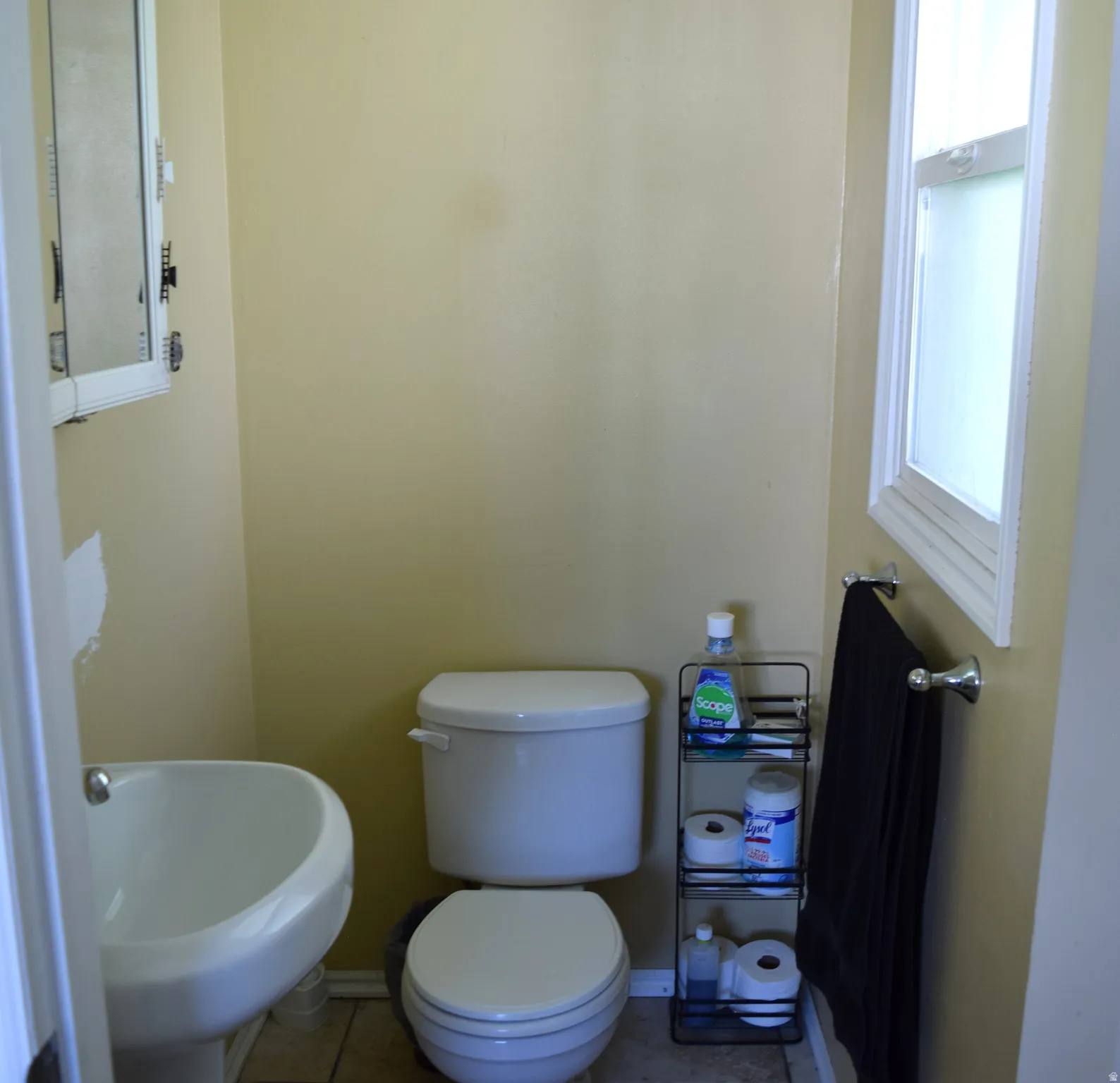 Compact bathroom featuring a white wall-mounted sink, a toilet, a framed medicine cabinet, a window with white trim, and tile flooring