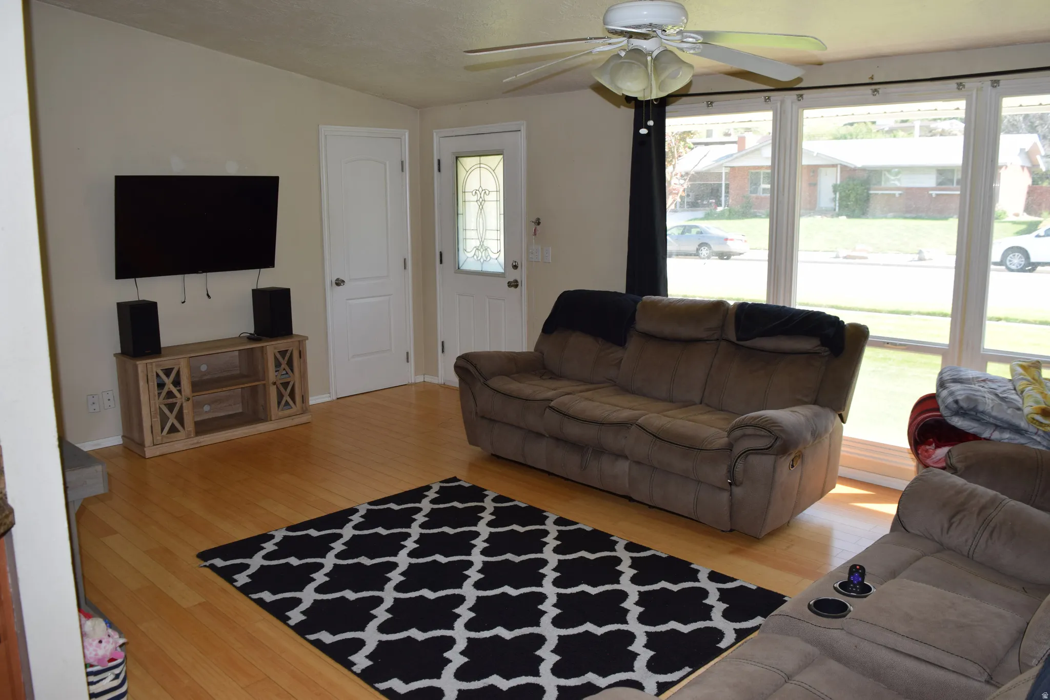 Living area featuring light wood-finish flooring, a white ceiling fan, and large picture windows
