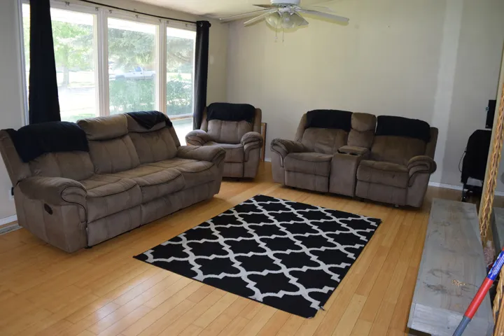 Bright living area featuring wood-finish flooring, a ceiling fan, and large windows with black drapery