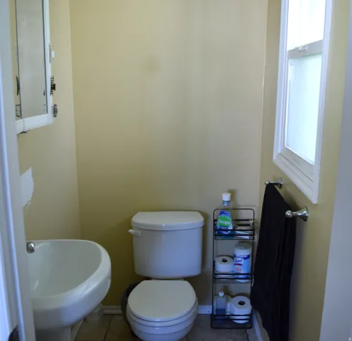 Compact bathroom featuring a white wall-mounted sink, a toilet, a framed medicine cabinet, a window with white trim, and tile flooring