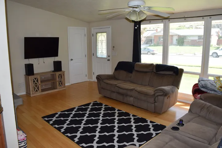 Living area featuring light wood-finish flooring, a white ceiling fan, and large picture windows