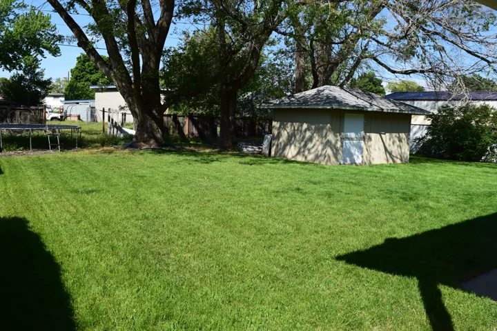Spacious green lawn with mature trees and a detached shed featuring a hip roof