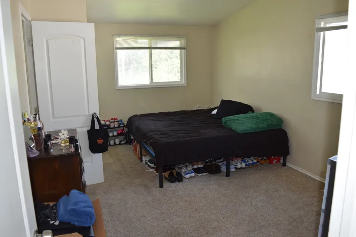Carpeted room with neutral-toned walls, featuring a window with white trim, a second window with white trim, and a white interior door