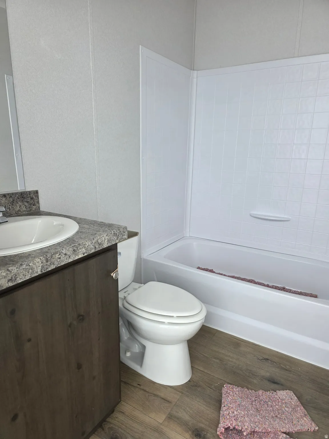 Bathroom featuring wood-finish flooring, a white porcelain toilet, and a bathtub with a white surround