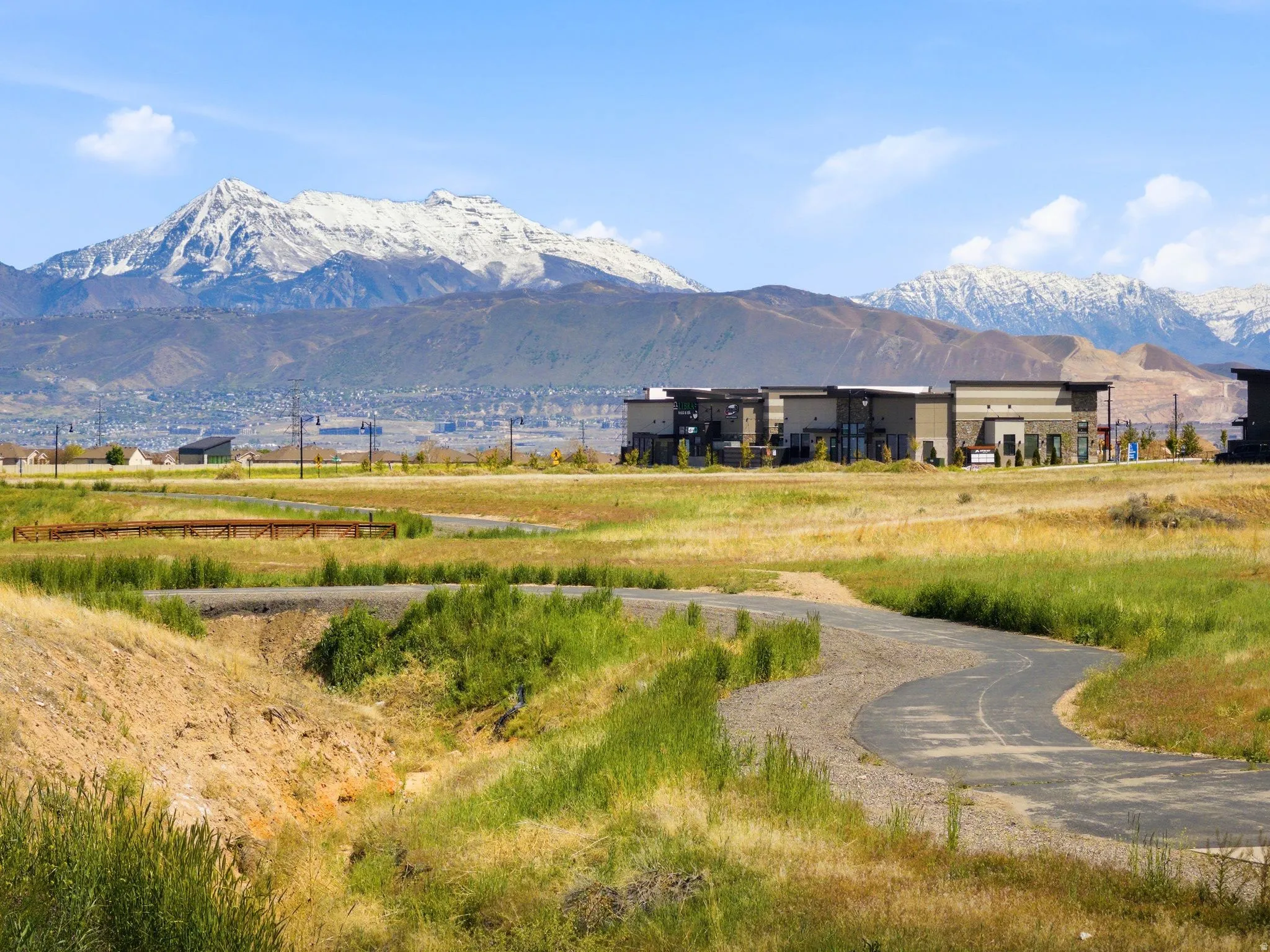 Paved pathway winding through open fields with distant snow-capped mountains