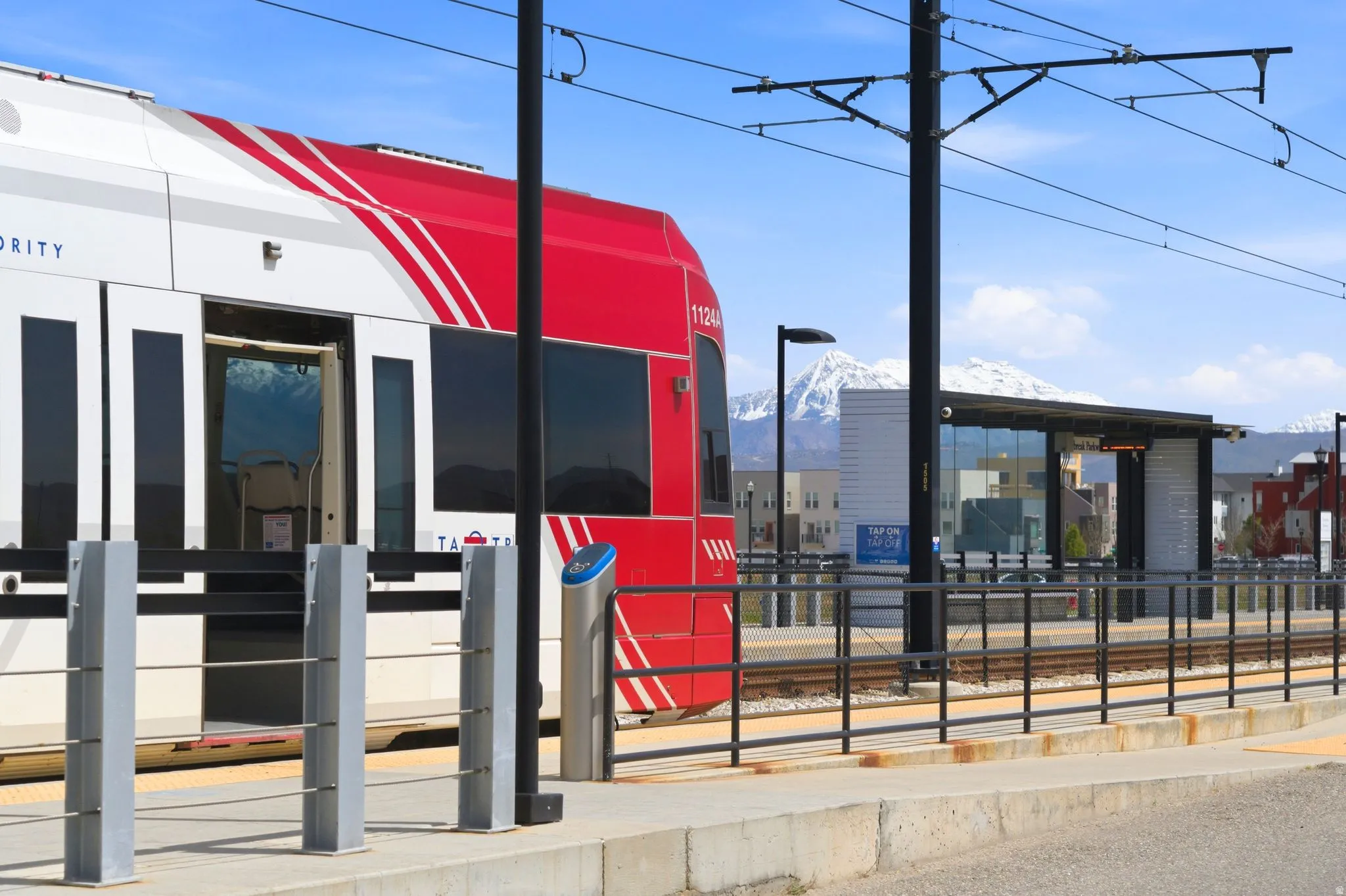 Modern light rail transit station featuring a red and white train, a glass-enclosed shelter, and clear sky conditions