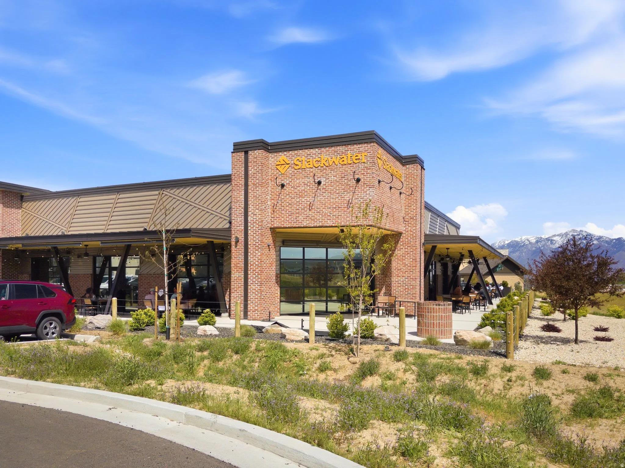 Brick exterior commercial building with local restaurant - Slackwater in the community with a covered outdoor patio, large glass windows, and a metal roof