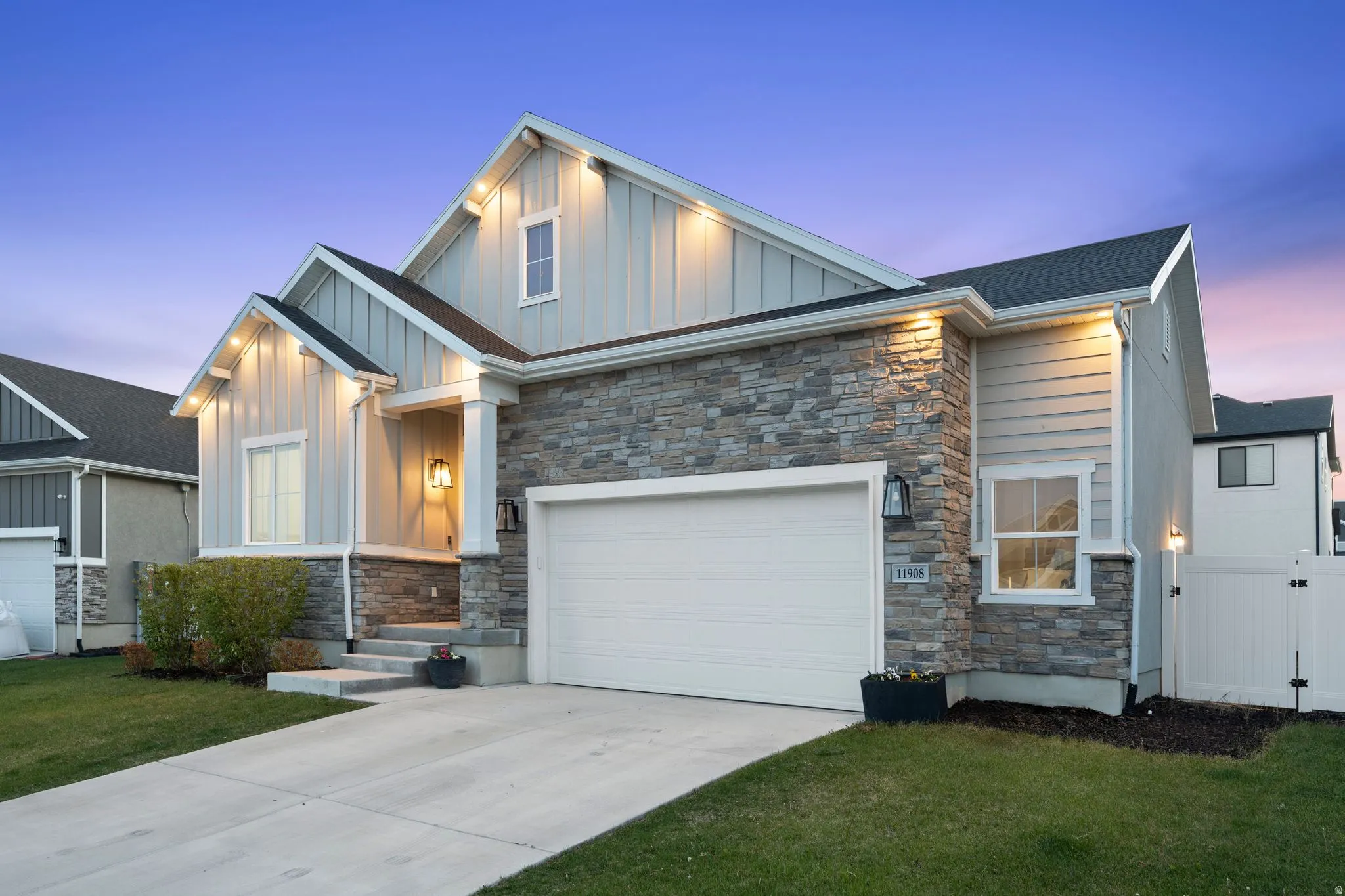 Contemporary exterior with a two-car garage, stone and board-and-batten siding, a covered entry, and a manicured lawn