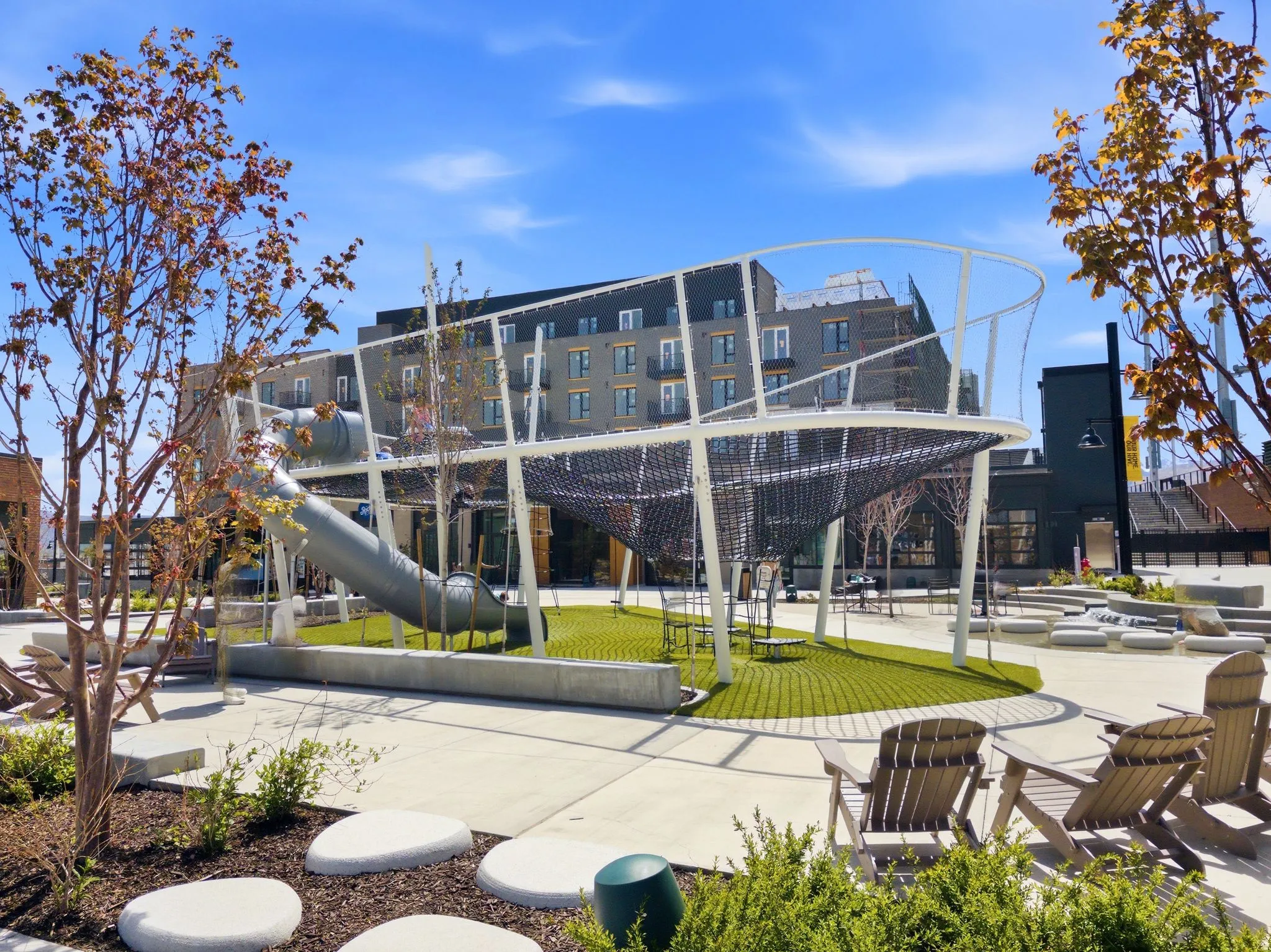 Outdoor recreation area featuring a modern play structure with a slide, artificial turf ground cover, and surrounding concrete pathways