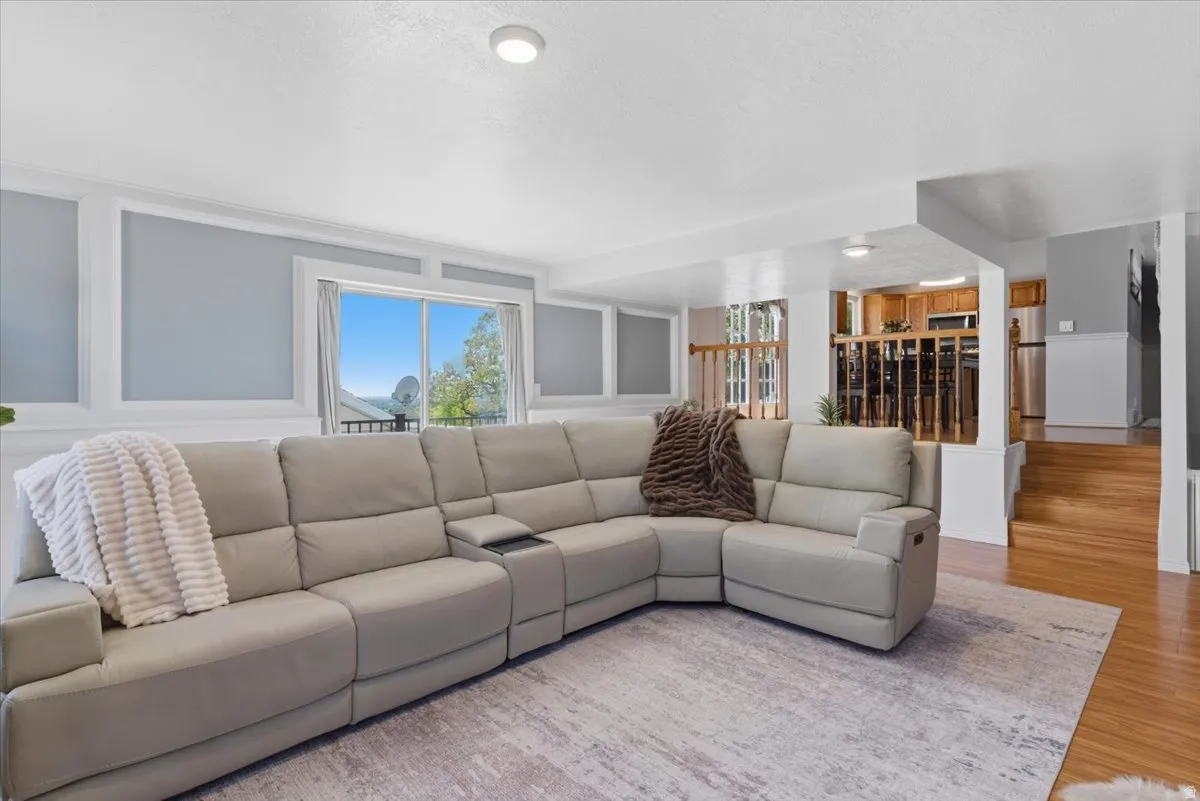 Living area featuring light gray walls with decorative white wainscoting, a large window, a light-colored area rug, recessed ceiling lighting, and wood-finish flooring