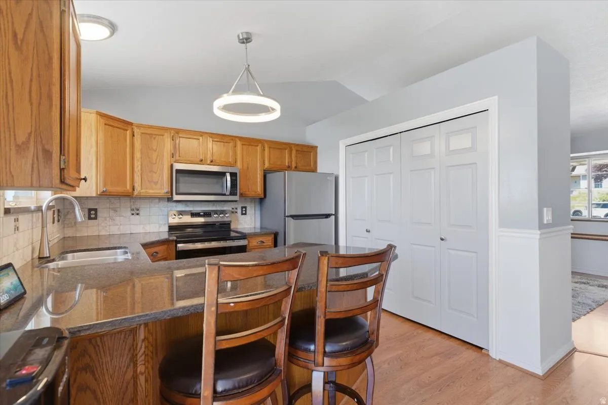 Kitchen featuring wood cabinetry, stainless steel appliances, a stone-finish countertop with an undermount sink, and a tile backsplash