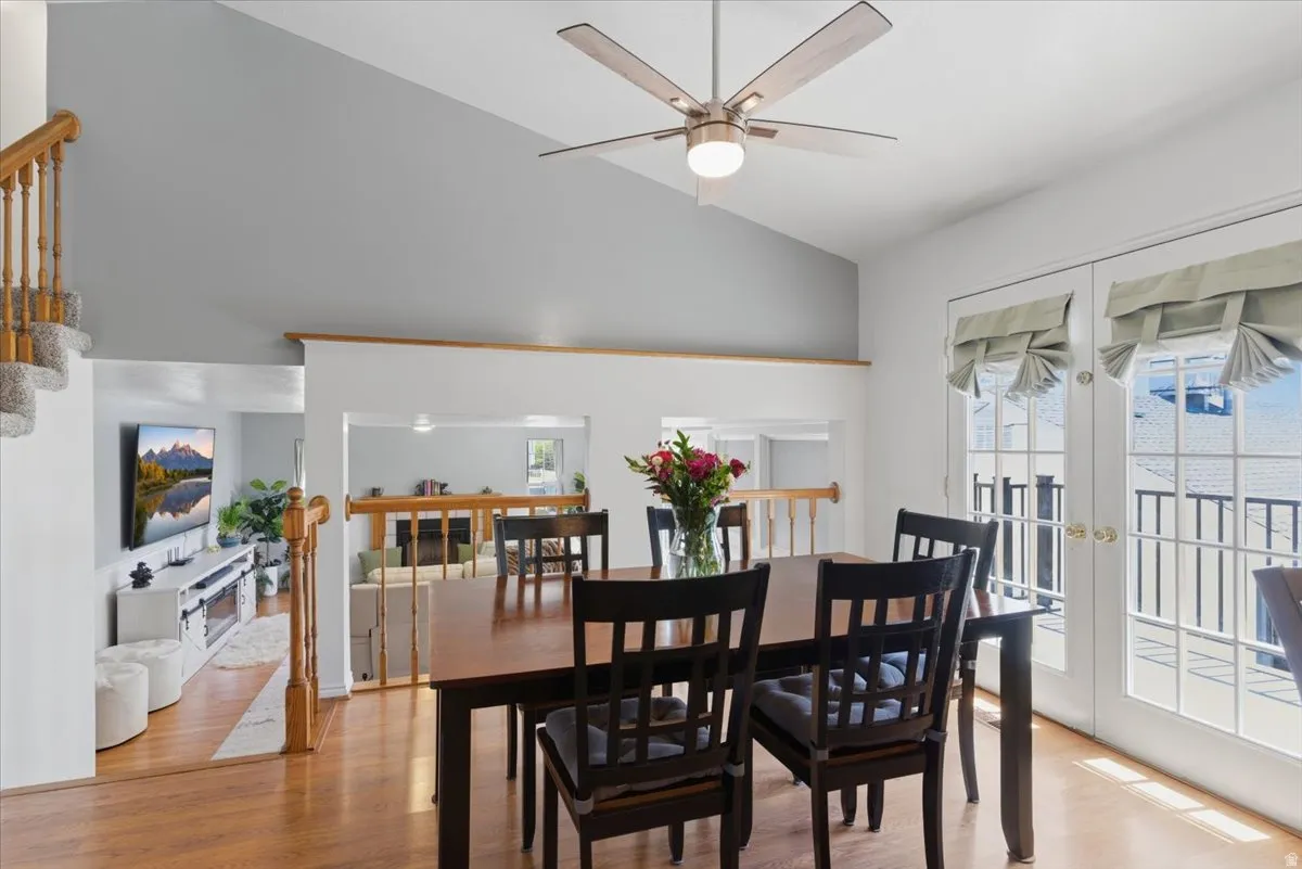 Dining area featuring wood-finish flooring, vaulted ceiling with a modern ceiling fan, and French doors with custom window treatments