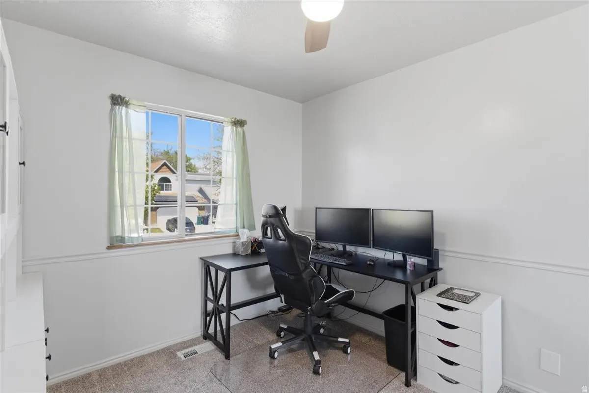 Bright room featuring a large window with white framing, neutral wall tones, textured carpeting, and a ceiling fan
