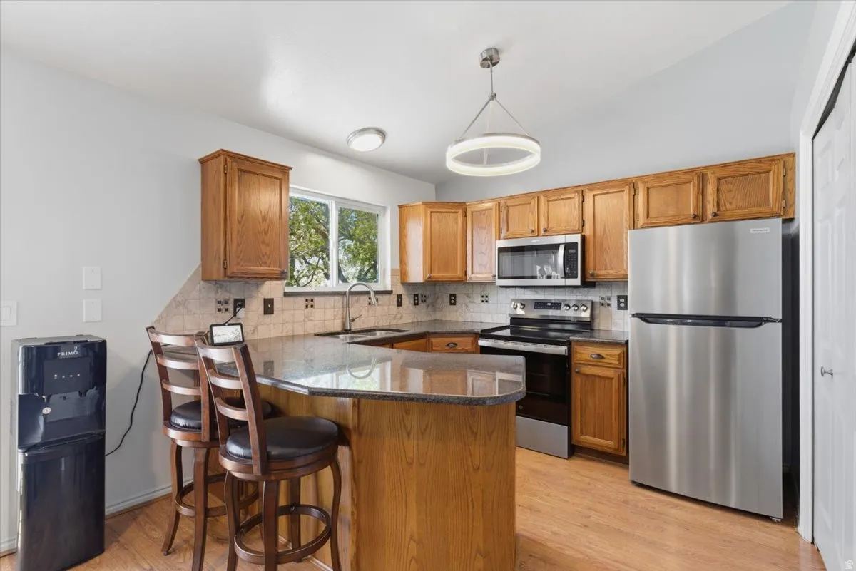 Kitchen featuring wood-finish flooring, a U-shaped island with seating, granite countertops, and a tiled backsplash