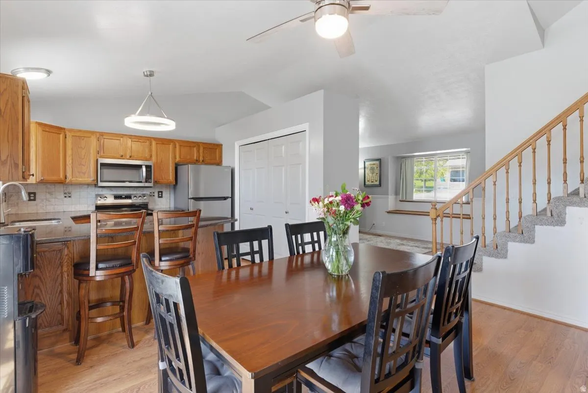 Kitchen and dining area featuring wood-finish flooring, wood cabinetry, a tile backsplash, and stainless steel appliances