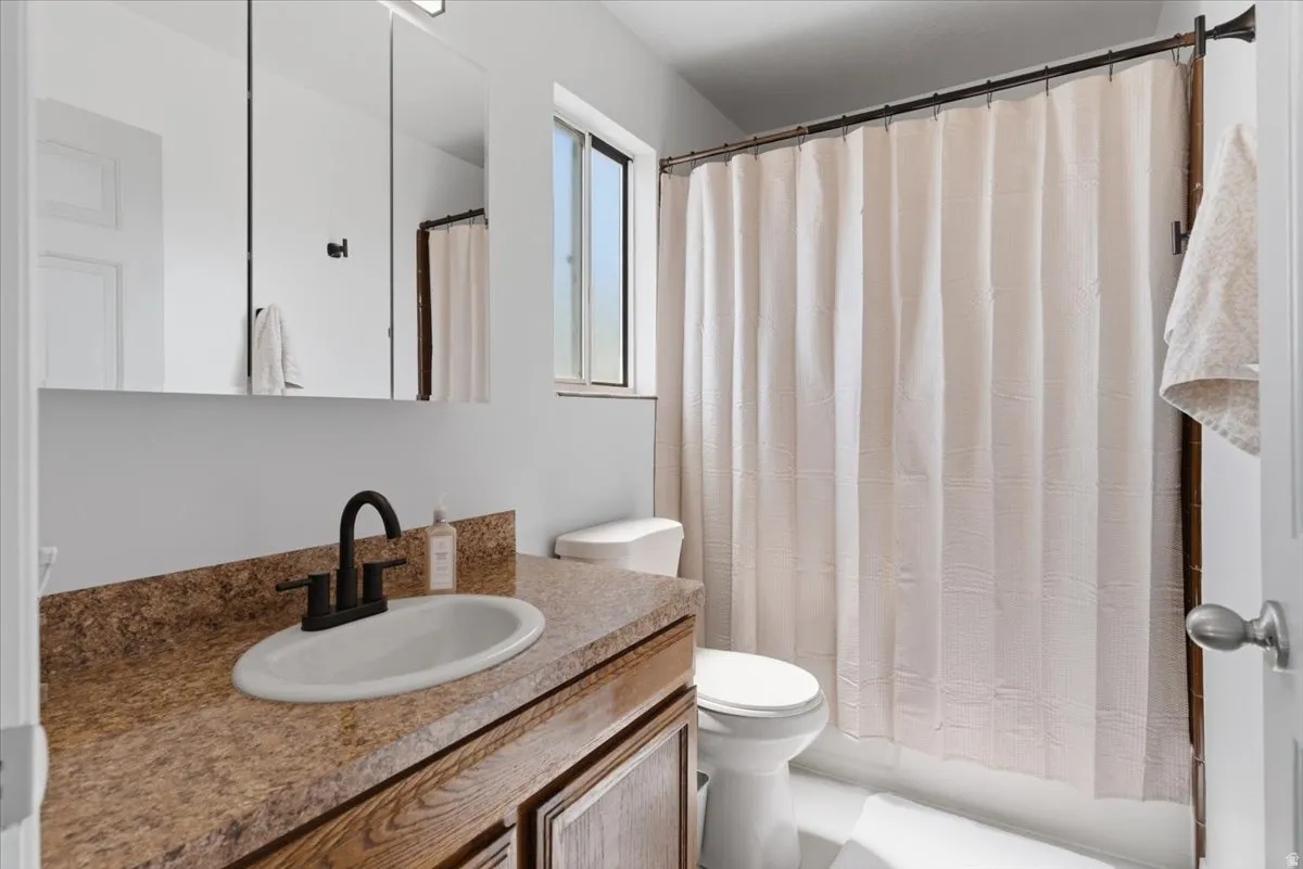 Bathroom featuring an integrated vanity sink with matte black hardware, wood-finish cabinetry, a three-panel mirrored medicine cabinet, a window, and a shower/tub combination