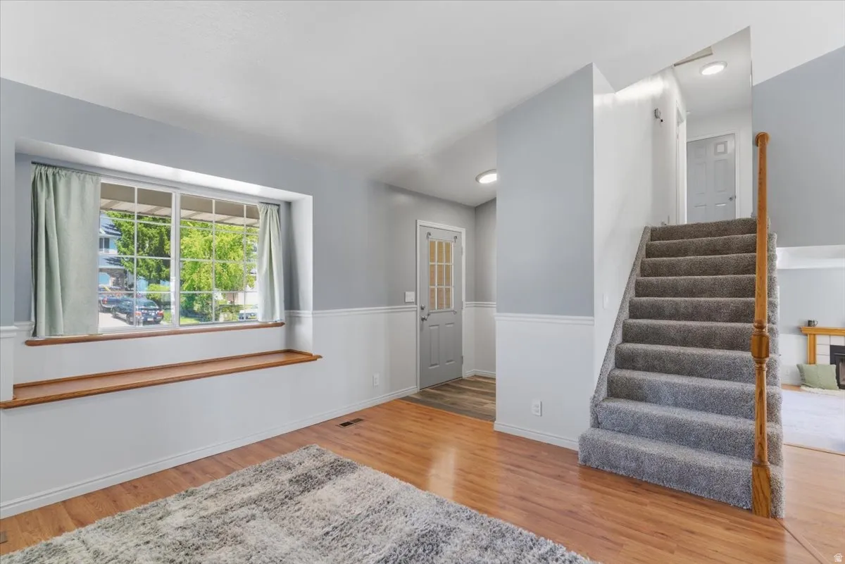 Spacious living area featuring wood-finish flooring, a broad bay window with a built-in wood window seat, and a carpeted staircase with a wood handrail