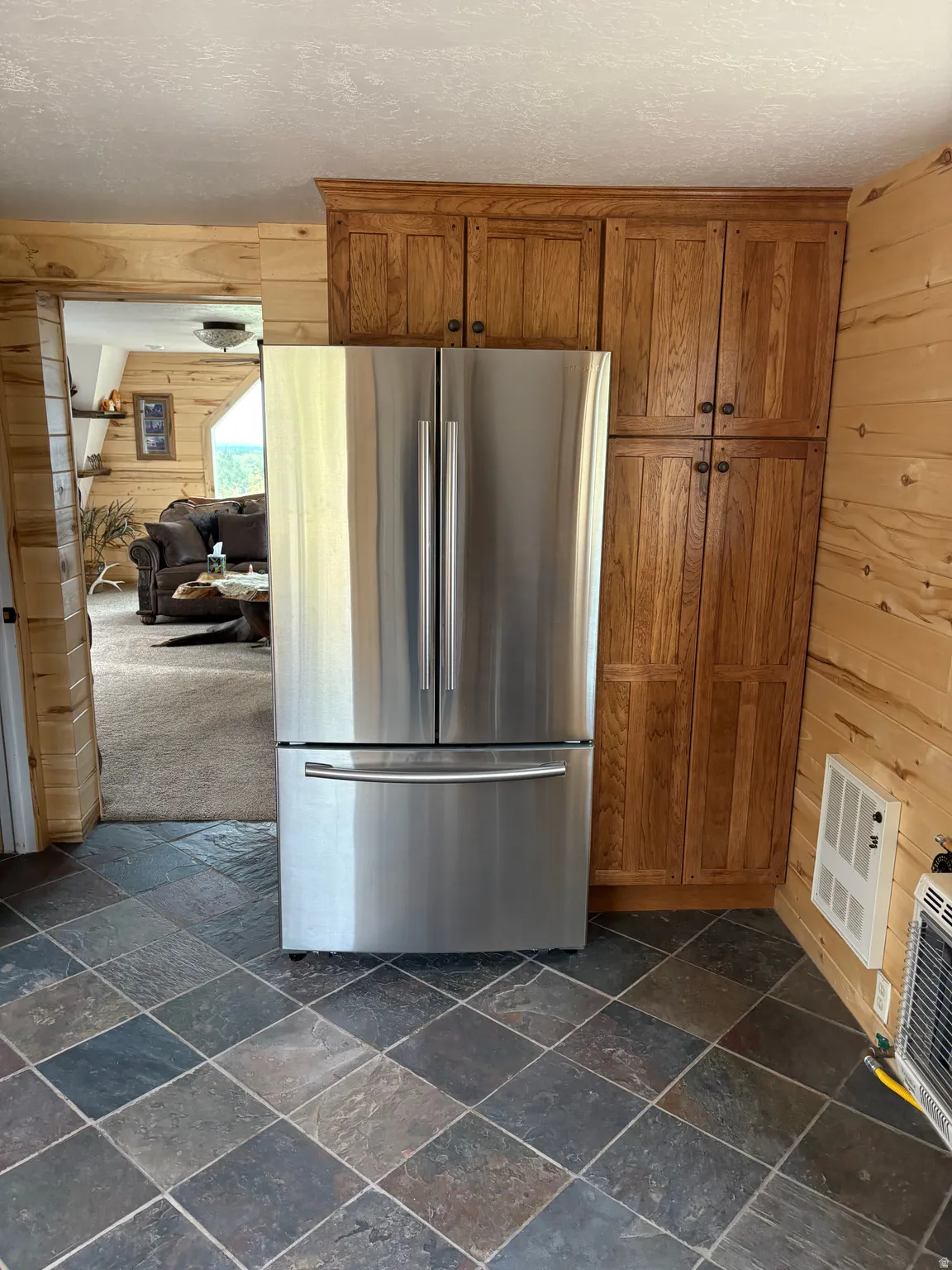 Stainless steel French door refrigerator with bottom freezer, set against natural wood-paneled walls and complementing wood cabinetry