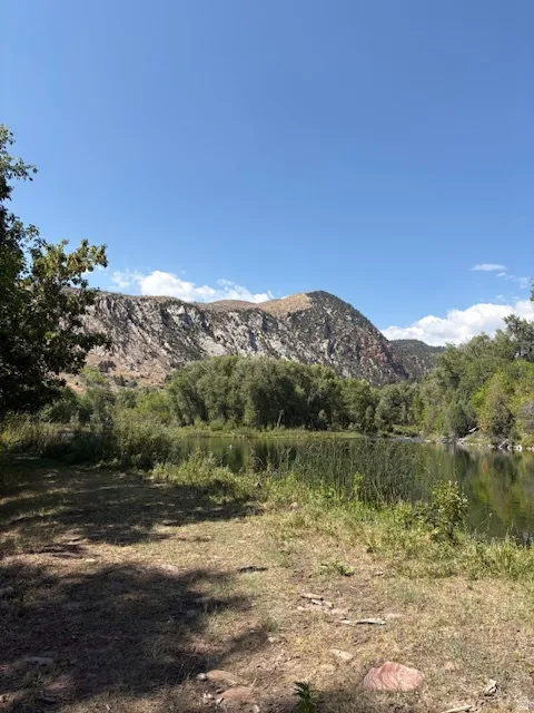 Natural landscape featuring a body of water, dense green foliage, and a prominent mountain range under a clear sky