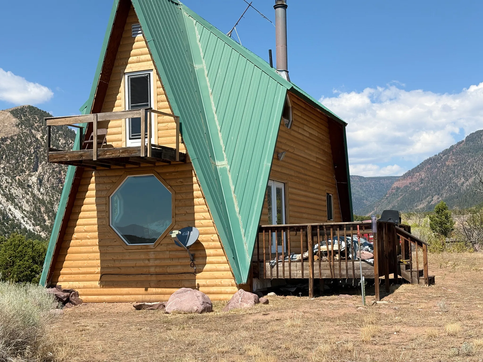 A-frame structure featuring a green metal roof, natural wood-finish siding, and an upper-level balcony