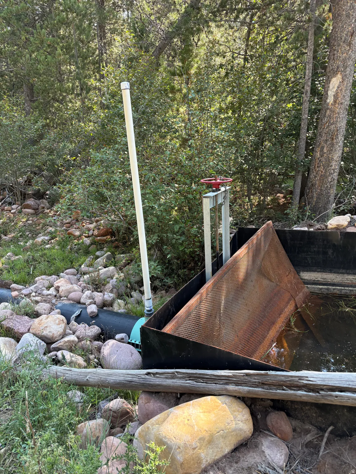 Water feature with an active flow, integrated with a large red valve, black piping, and a metal grate