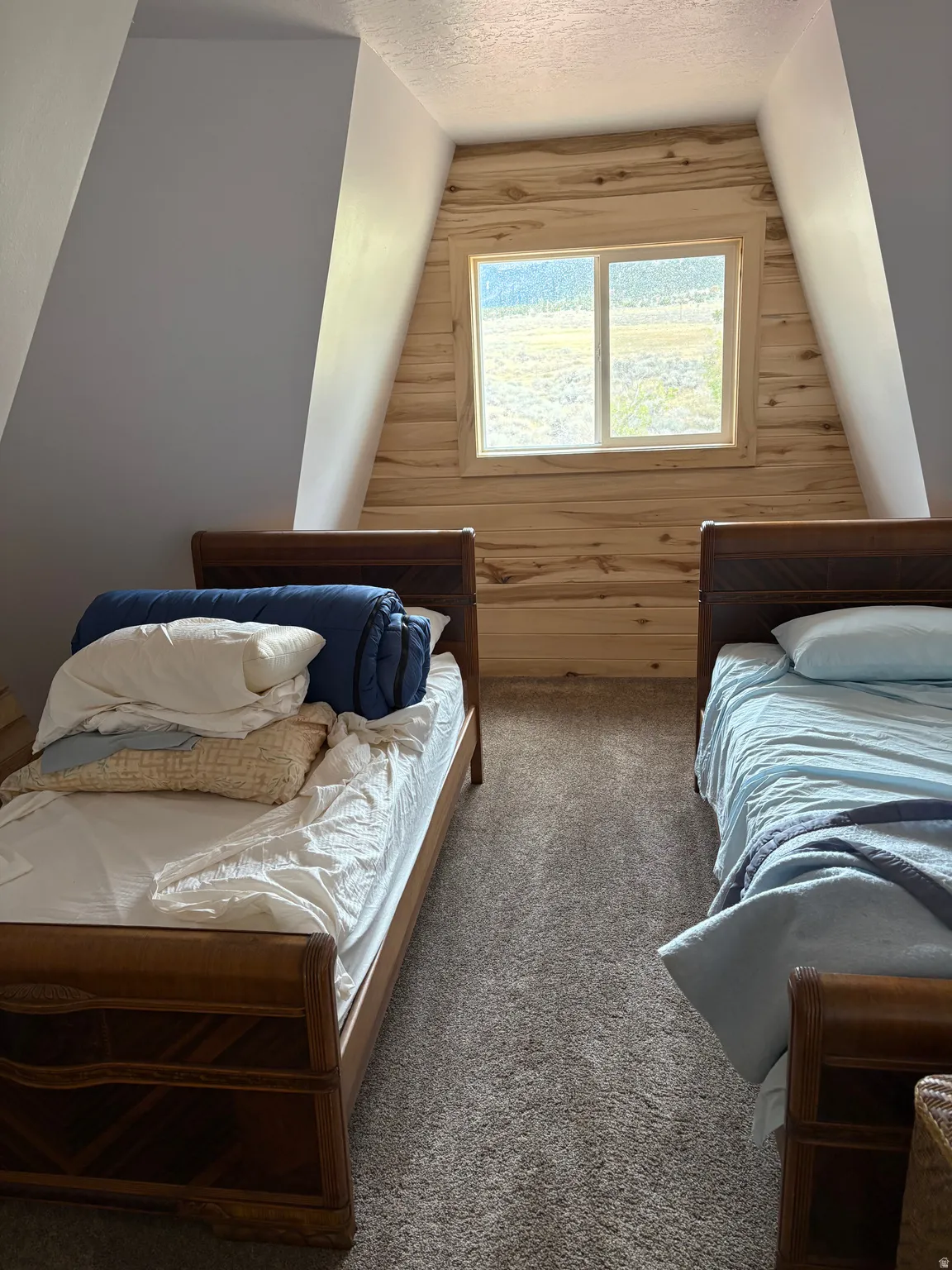 Attic space featuring sloped walls, a central window with wood-finish trim, and natural wood paneling