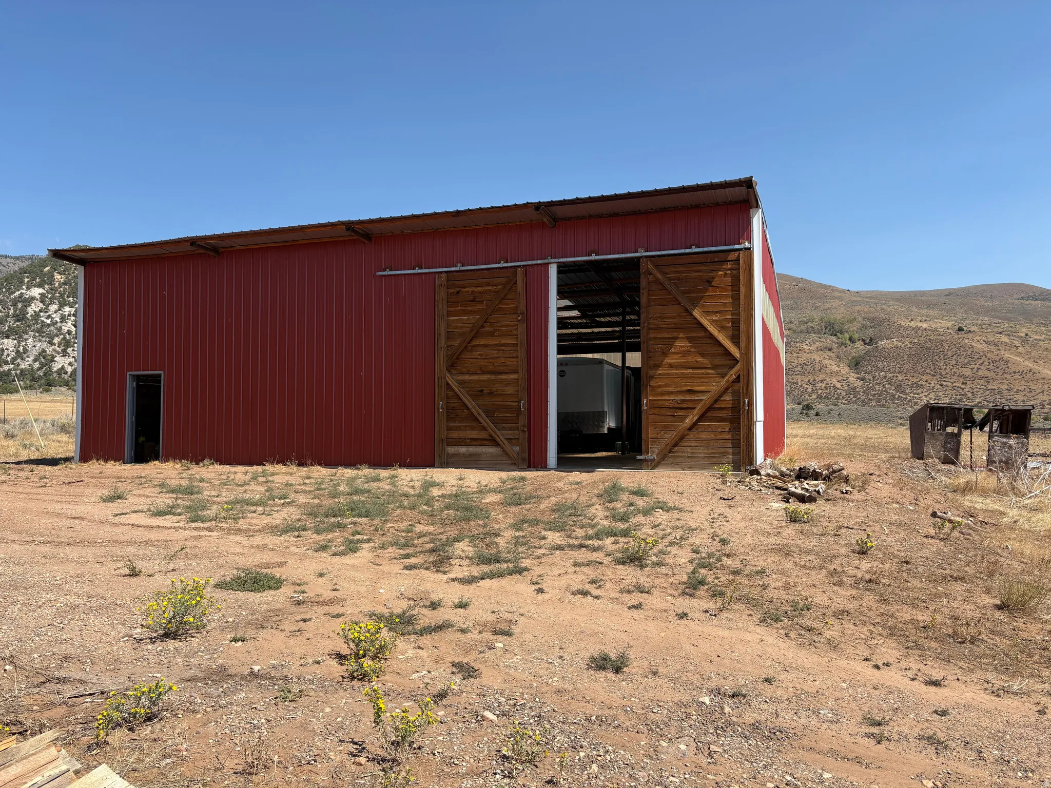 Red metal barn structure featuring a galvanized roof, a single entry door, and large sliding wood doors
