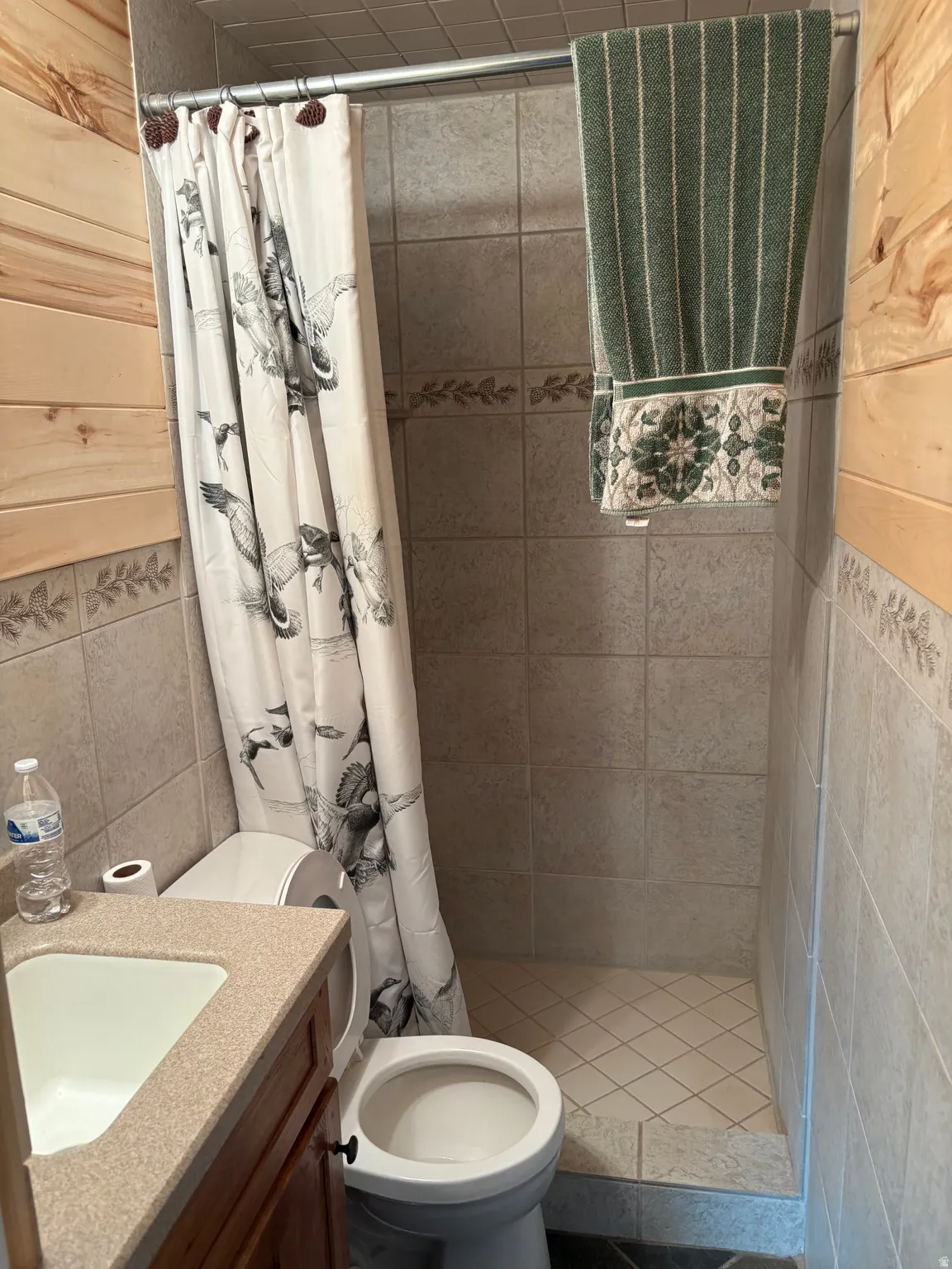 Bathroom featuring a shower with tile surround and floor, vanity with integrated sink, and wood-finish paneling