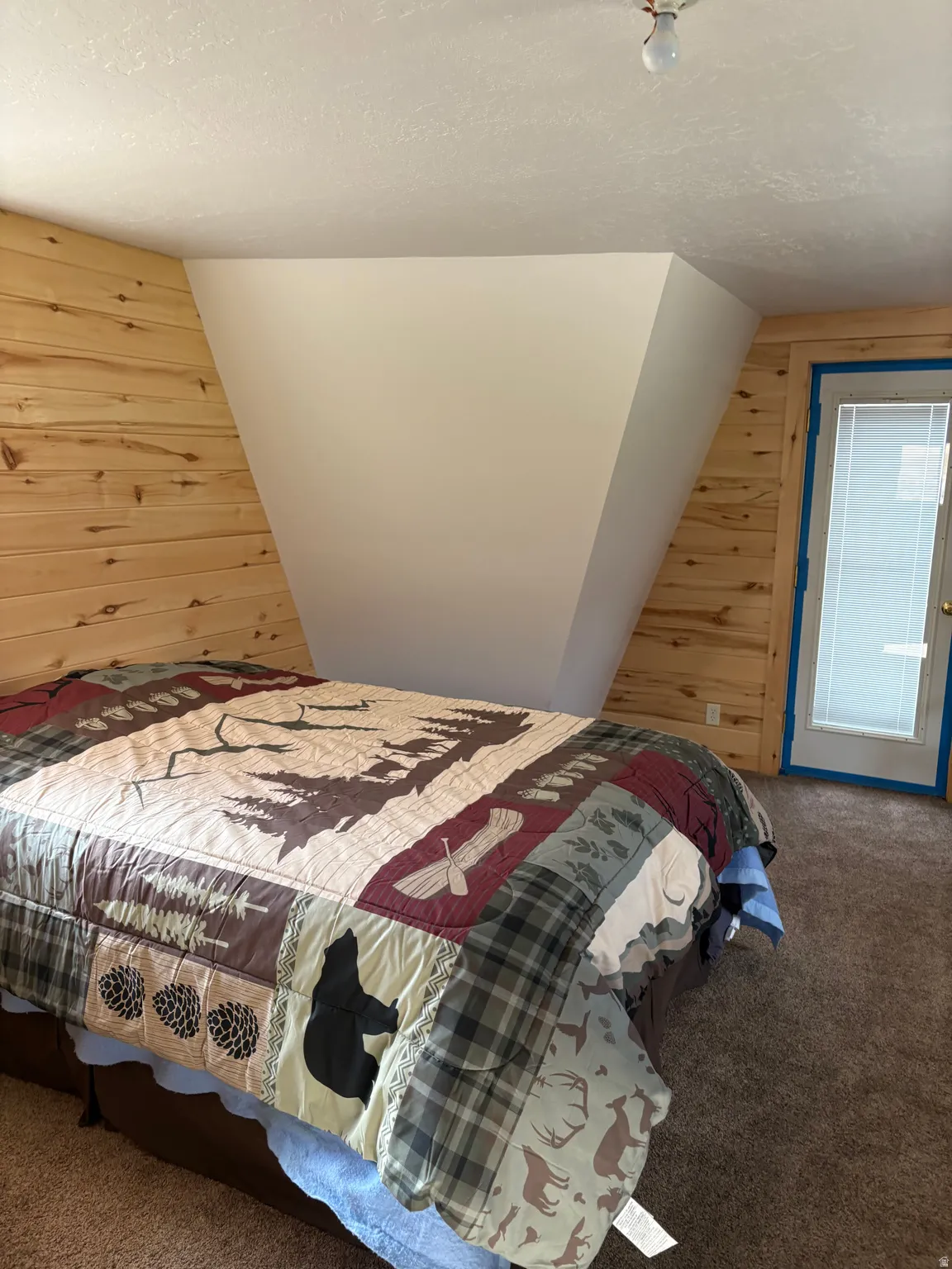 Interior room featuring a wood plank accent wall, textured ceiling, brown carpet flooring, and an exterior door with integrated blinds