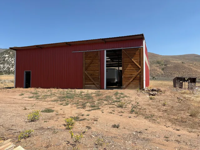 Red metal barn structure featuring a galvanized roof, a single entry door, and large sliding wood doors