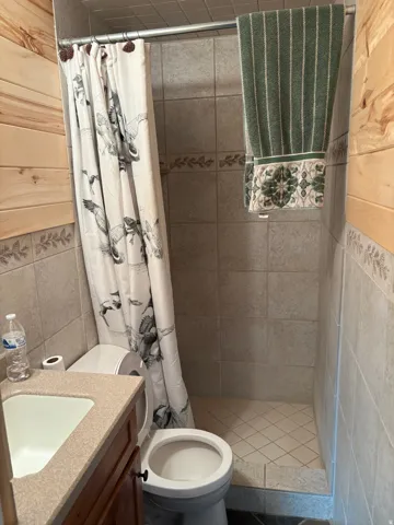 Bathroom featuring a shower with tile surround and floor, vanity with integrated sink, and wood-finish paneling