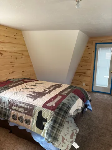 Interior room featuring a wood plank accent wall, textured ceiling, brown carpet flooring, and an exterior door with integrated blinds