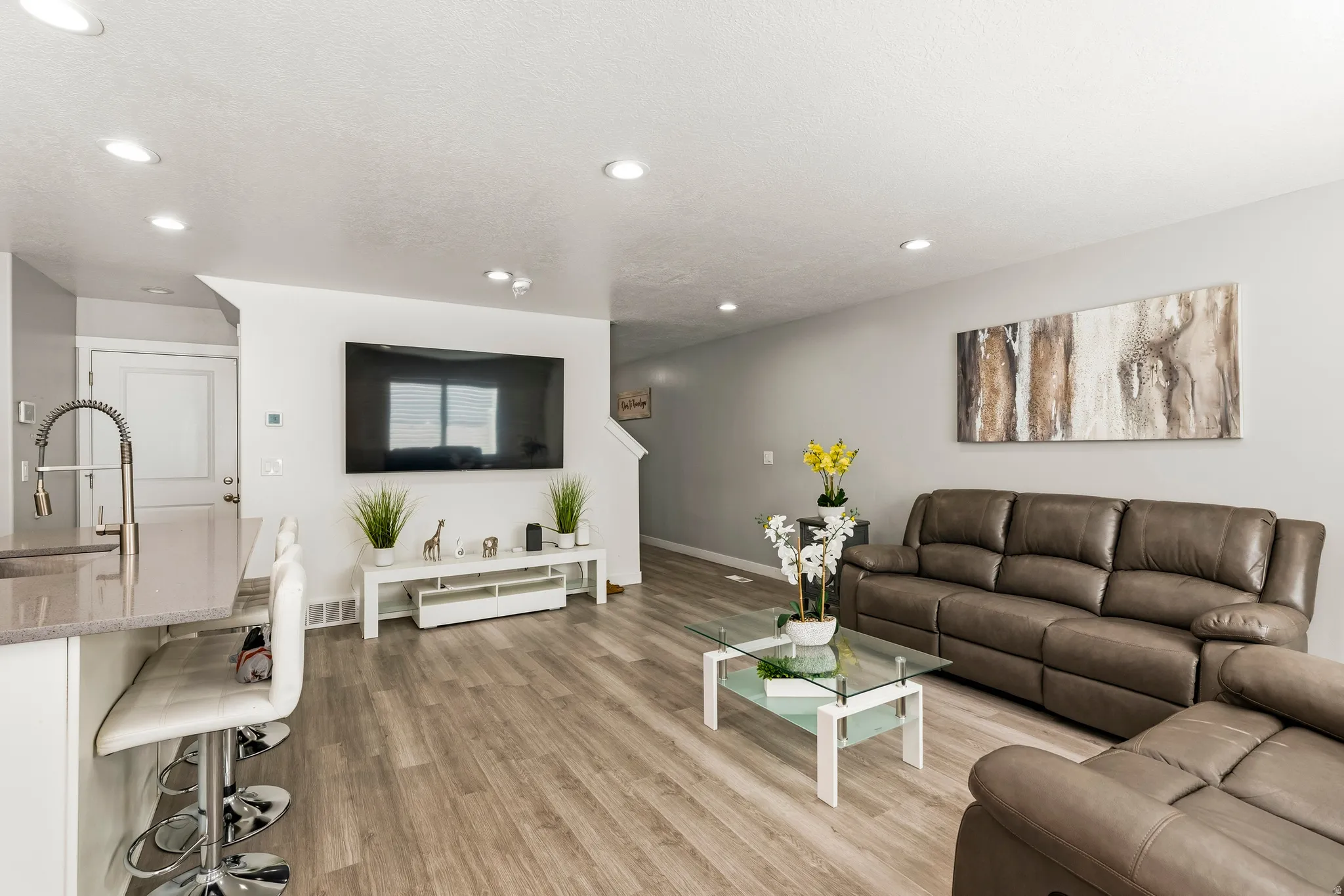 Open-concept living area featuring recessed lighting, light wood-finish flooring, and a kitchen island with a gooseneck faucet