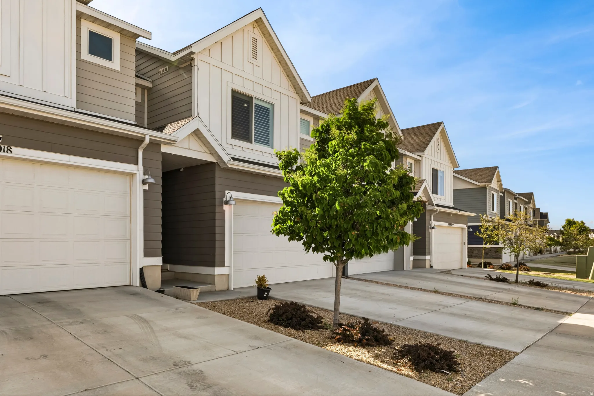 Modern townhome exterior featuring contemporary siding, white garage doors, gabled rooflines, and individual driveways