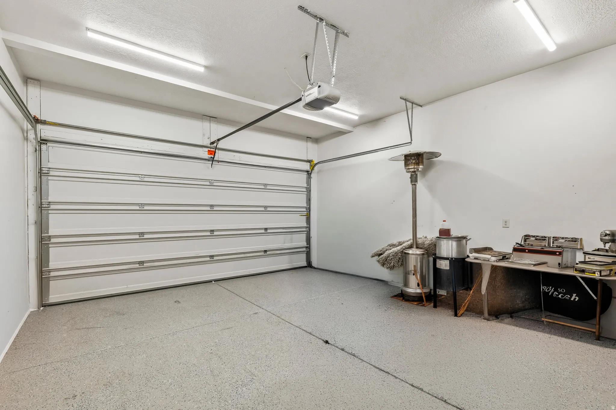 Spacious garage featuring a sectional garage door, automatic opener, textured concrete flooring, and overhead strip lighting