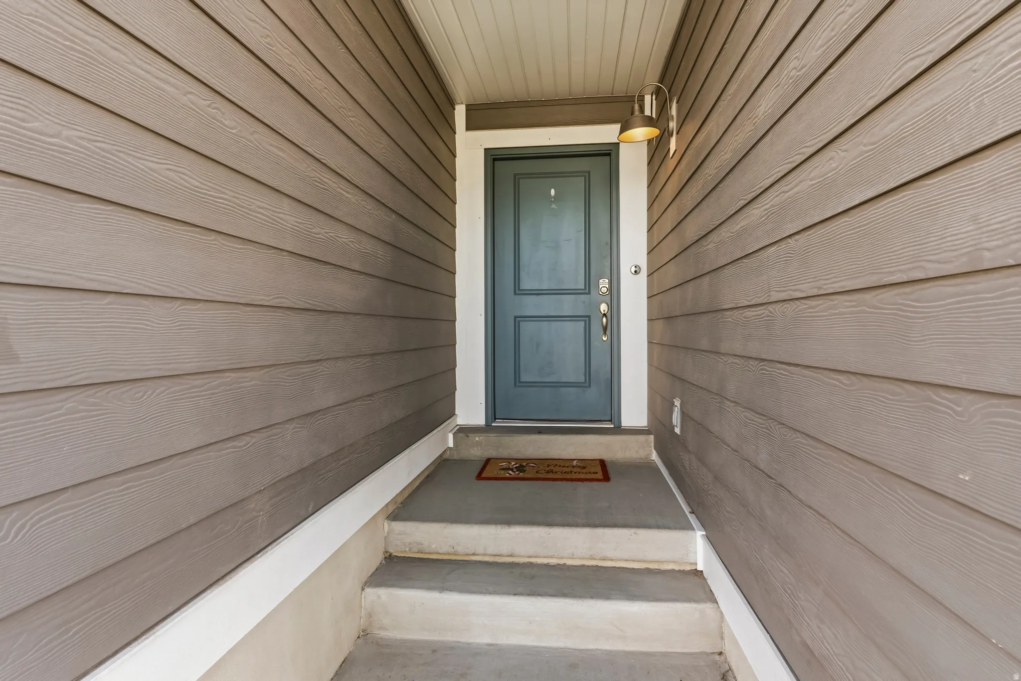 Entryway featuring horizontal siding in a neutral tone, a deep blue main door with classic paneling, and a contemporary wall-mounted light fixture