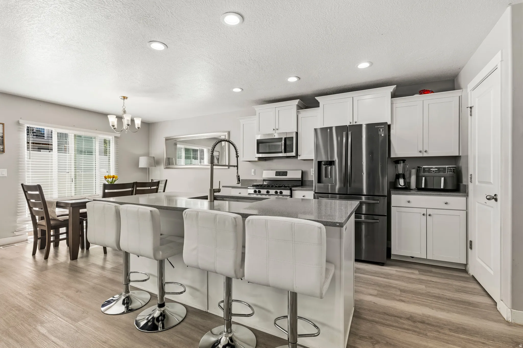 Open-concept kitchen with white shaker cabinetry, stainless steel appliances, and a central island with countertop seating