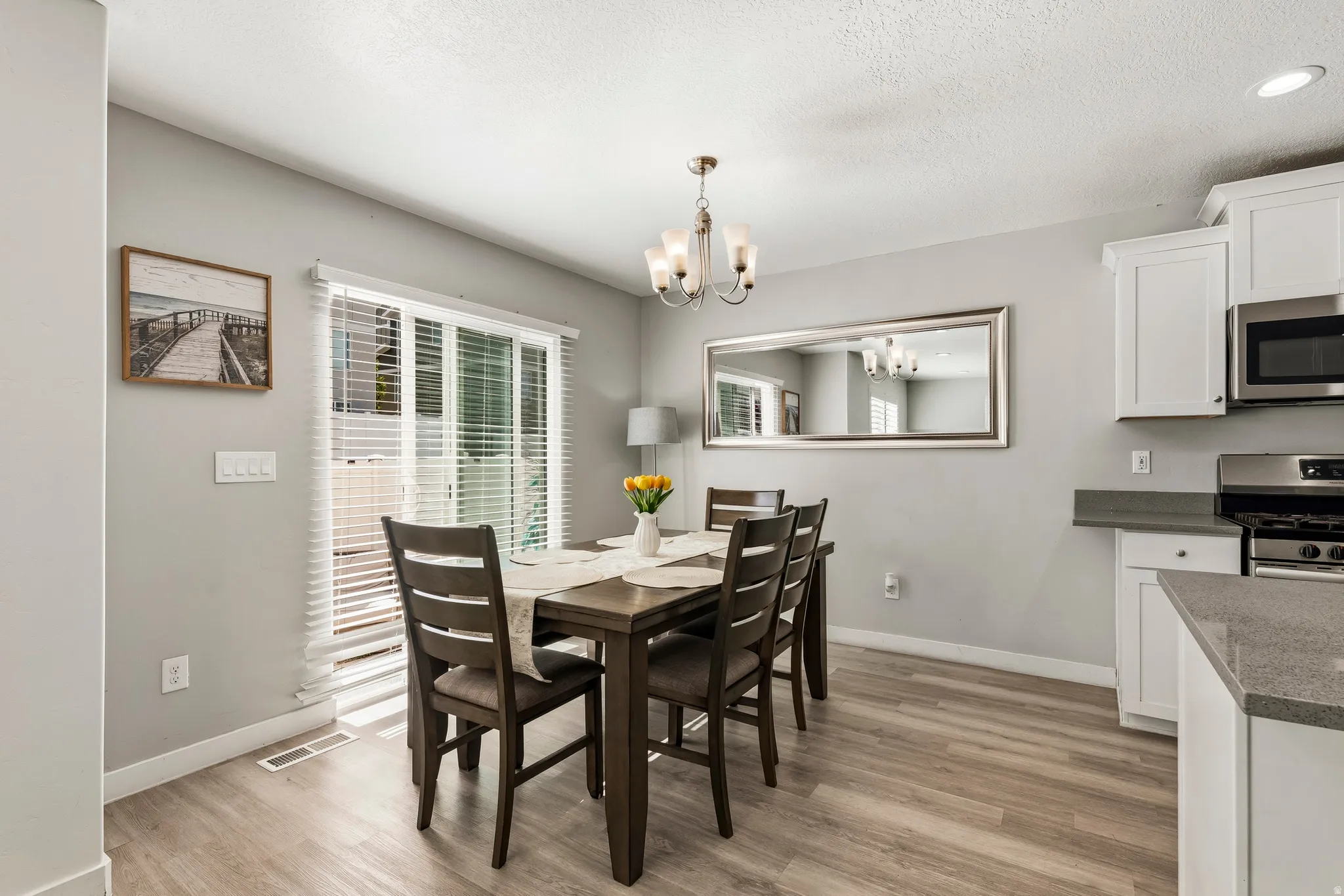 Dining area featuring wood-finish flooring, a sliding glass door, overhead chandelier lighting, white cabinetry, and gray countertops
