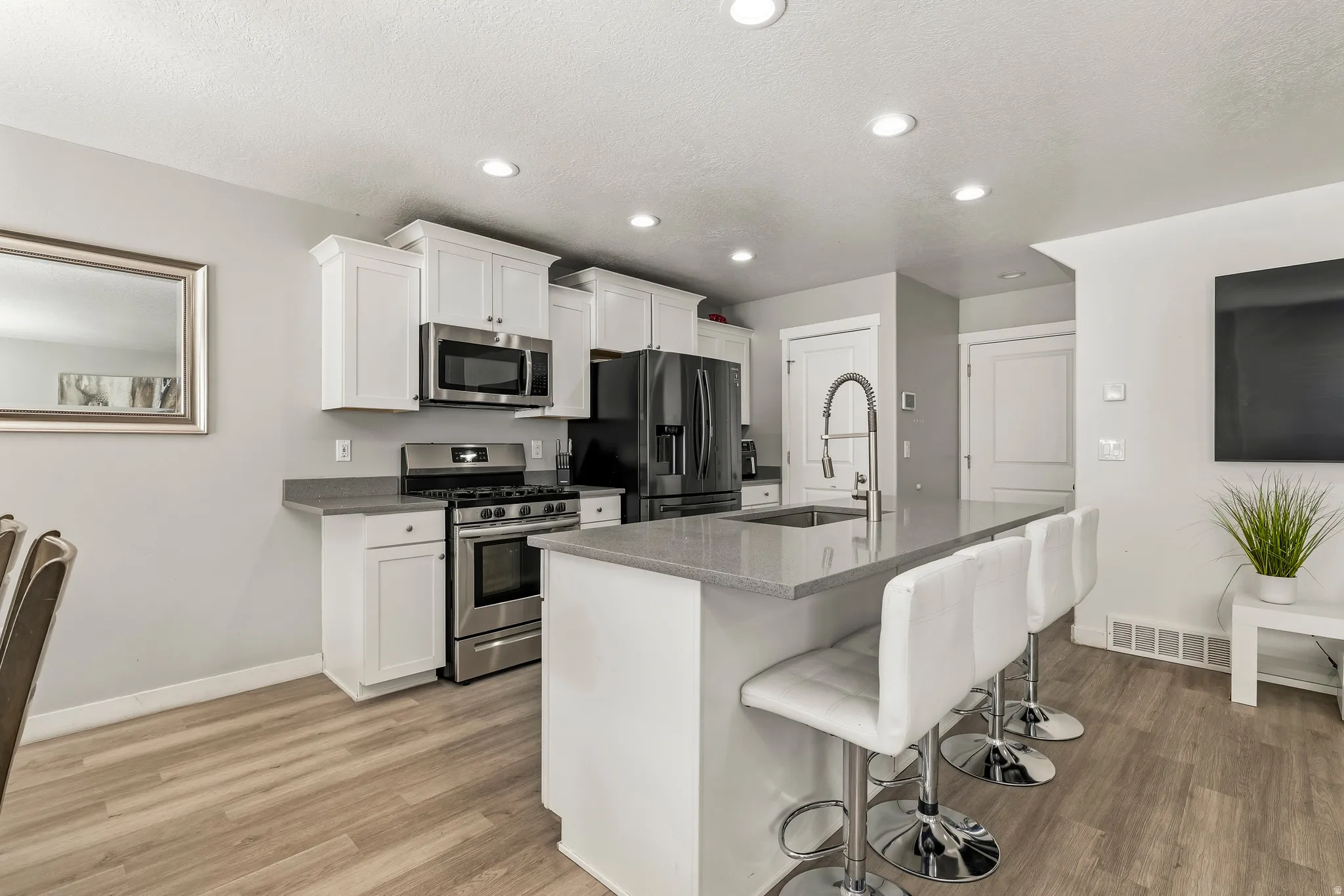 Kitchen featuring white cabinetry, stainless steel appliances, a center island with a sink, light gray countertops, and wood-finish flooring