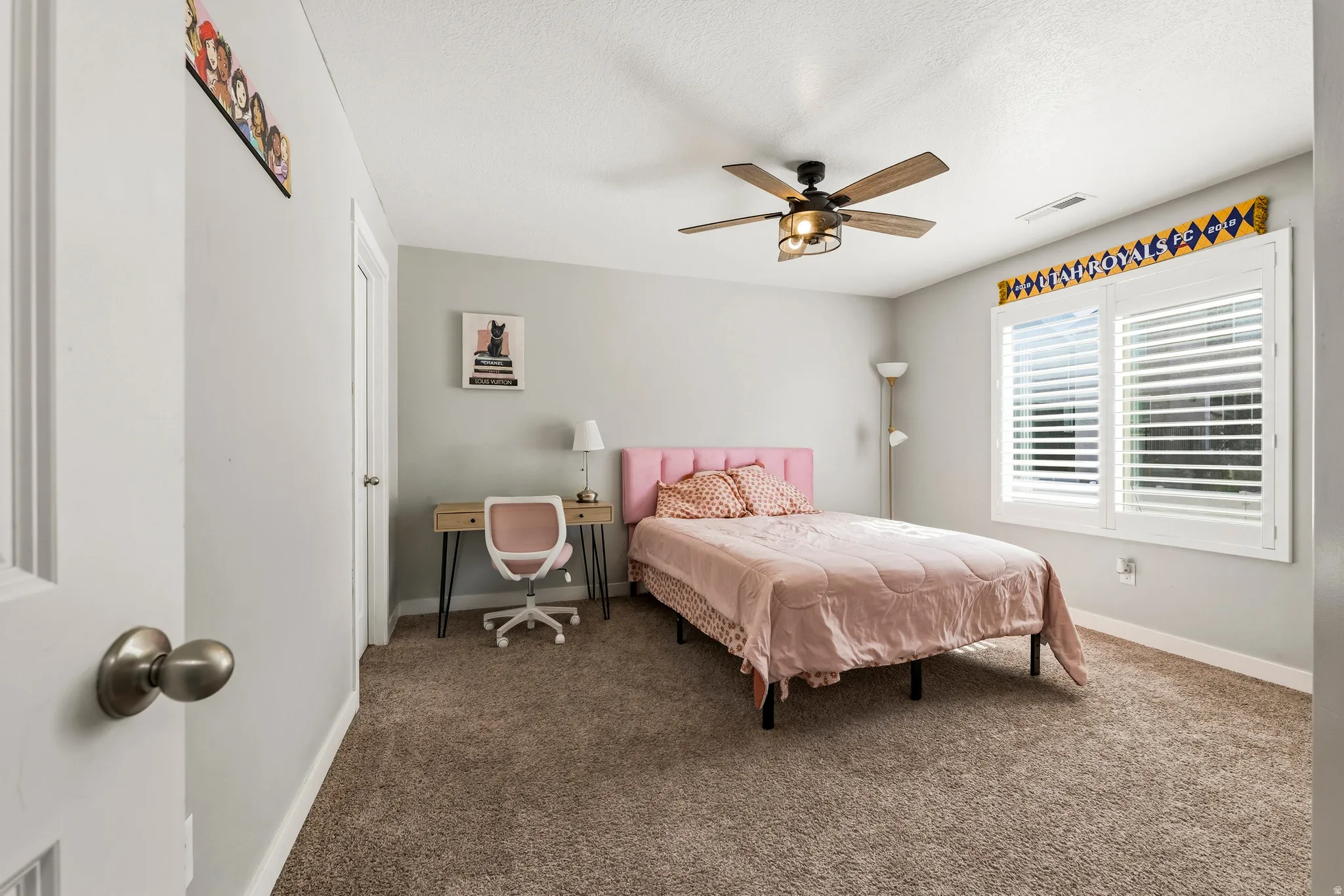 Carpeted room featuring a ceiling fan with light fixture, window with white plantation shutters, and light gray wall paint