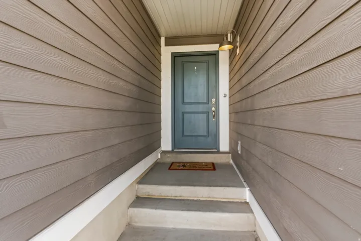 Entryway featuring horizontal siding in a neutral tone, a deep blue main door with classic paneling, and a contemporary wall-mounted light fixture