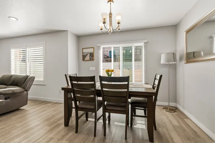 Dining area with wood-finish flooring, two window openings with horizontal blinds, and a brass-tone chandelier