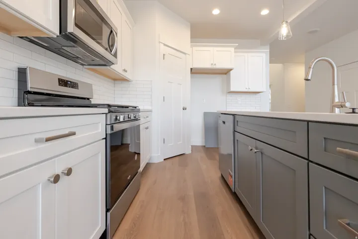 Kitchen featuring wood-finish flooring, two-tone cabinetry, stainless steel appliances, a subway tile backsplash, and recessed lighting