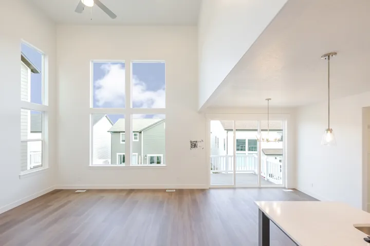 Vaulted ceiling with ceiling fan, expansive window array, wood-finish flooring, sliding glass door access to exterior deck, and pendant lighting
