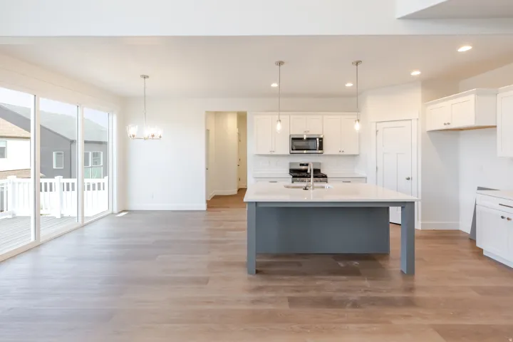 Open-concept living area featuring wood-finish flooring, a kitchen island with a sink, white cabinetry, stainless steel appliances, and sliding glass doors leading to an exterior deck