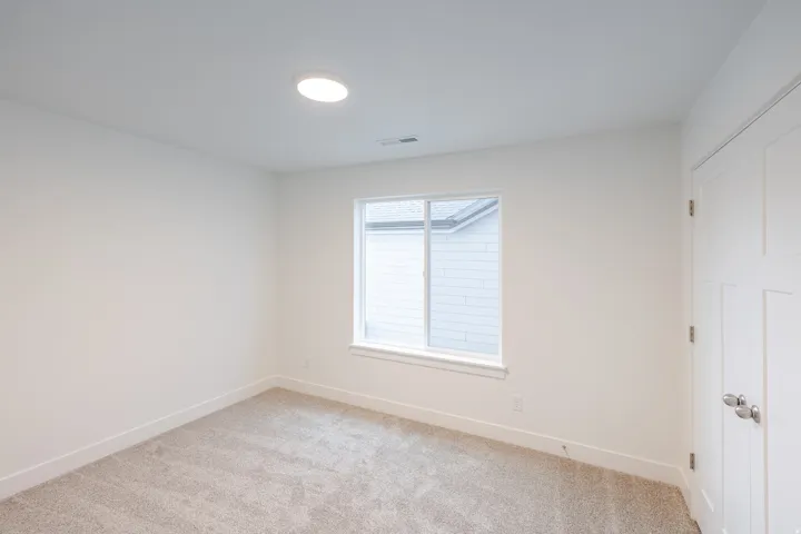 Recessed ceiling light, white walls, light-colored carpet, window with white trim, and a white interior door