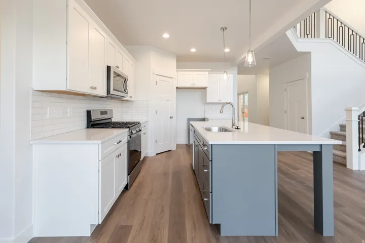 Kitchen featuring white shaker cabinetry, stainless steel appliances, a subway tile backsplash, and an island with a built-in sink and pendant lighting