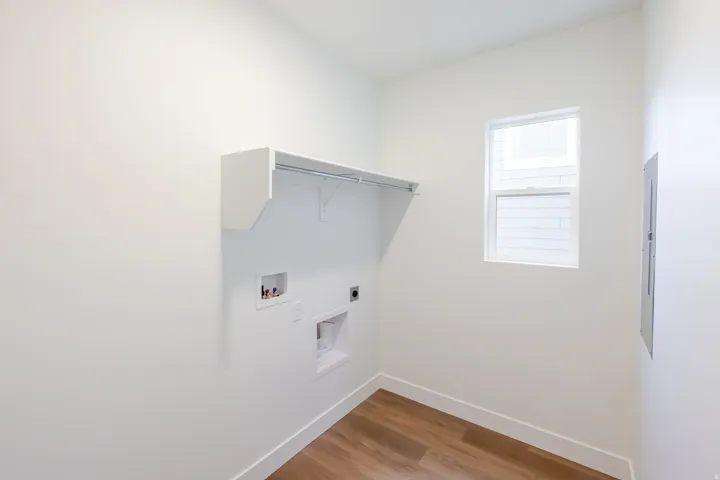 Laundry area with wood-finish flooring, a white wall-mounted shelf, and a window
