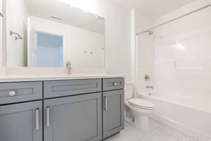 Spacious bathroom featuring a white bathtub/shower combination, light gray vanity with ample storage, a white countertop, and modern brushed nickel fixtures