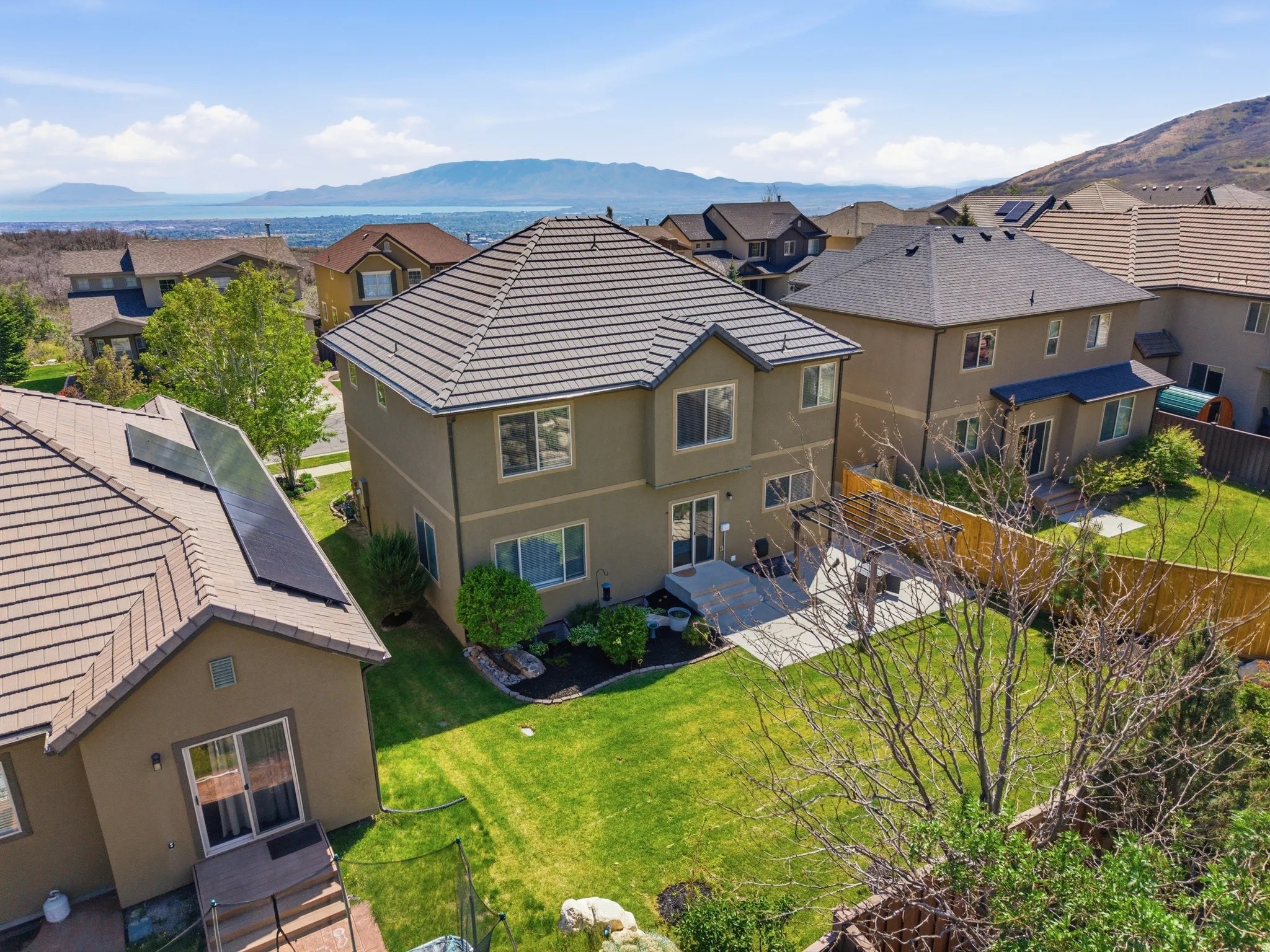 Expansive rear yard featuring a manicured lawn, concrete patio, mature tree, and privacy fencing